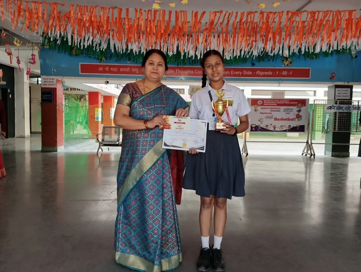 A woman and a schoolgirl in uniform stand in a school corridor, the girl holding a golden trophy and the woman holding a certificate at Bhavan's BVM Ashti.