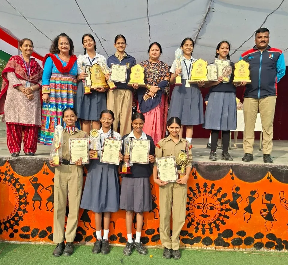 Group photo of students and staff on a stage holding trophies and certificates from All India Multilingual Dance competition, Bhavan's BVM Ashti