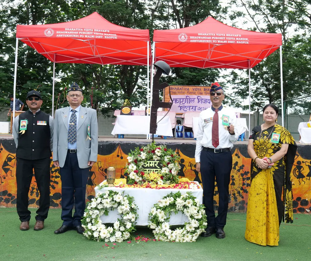 Bhavan's BVM Ashti: Four people in uniforms and formal clothes stand beside a floral tribute and wreaths under red tents on an outdoor ground.