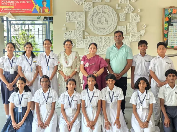 Posed group photo of about 15 students in school uniforms with three adults standing in front of a decorative wall relief indoors. - Bhavan's BVM Ashti