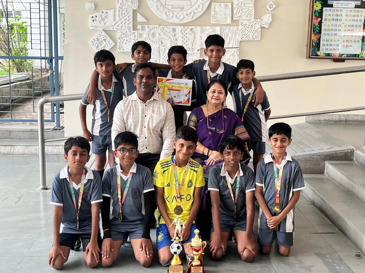 Group photo of a man, a woman and about nine boys in sports uniforms posing indoors with medals, a certificate and football trophies. - Bhavan's BVM Ashti
