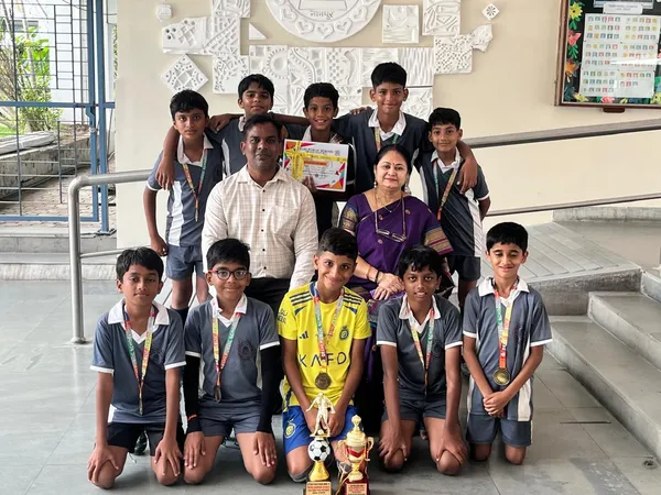 Group photo of a man, a woman and about nine boys in sports uniforms posing indoors with medals, a certificate and football trophies. - Bhavan's BVM Ashti
