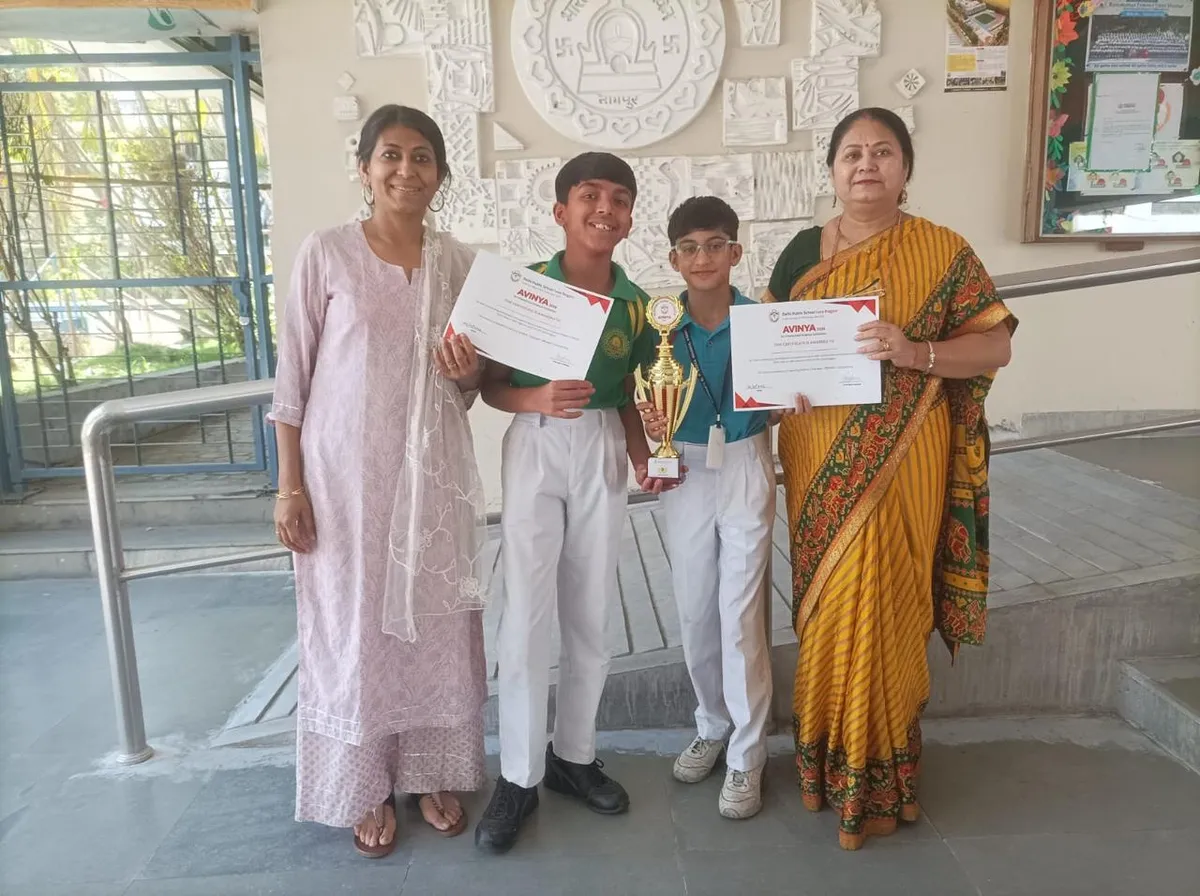 Two women and two schoolboys stand in a school corridor, the boys holding certificates and a golden trophy, facing the camera.