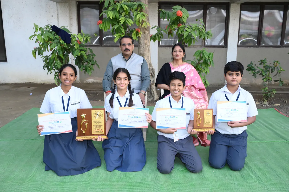 Group photo of four students holding certificates and two plaques, with a man and a woman seated behind them outdoors on a green mat.