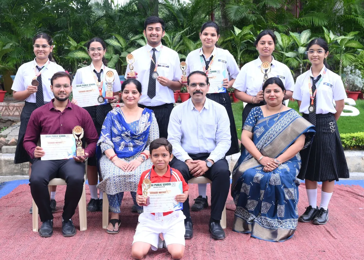 Group photo of students and adults posed outdoors on a red carpet, holding trophies, medals and certificates. - Bhavan's BVM SKN