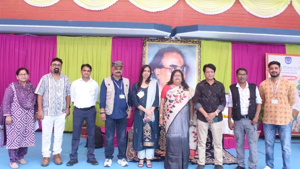 Group photo of nine adults standing in a row on a stage in front of colorful curtains and a framed portrait at CPS (Katol Road)