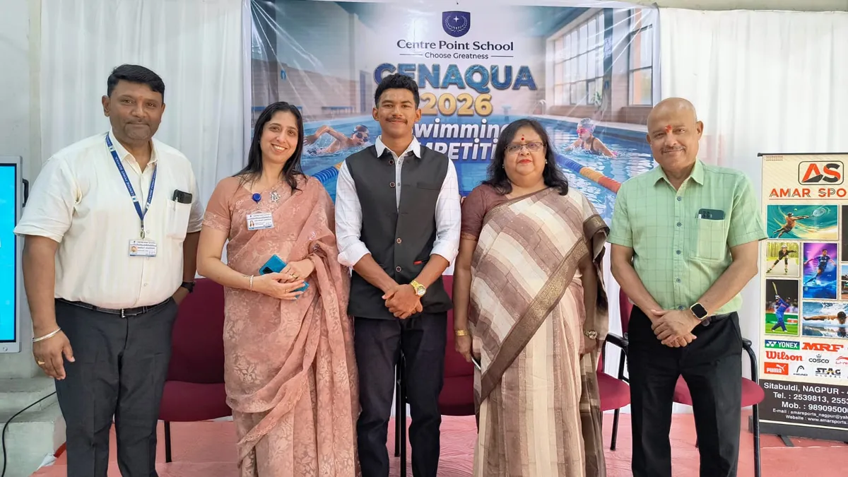 Five adults, four standing around a young man in a vest, pose in front of a swimming competition banner at an indoor event. - CPS (Katol Road)