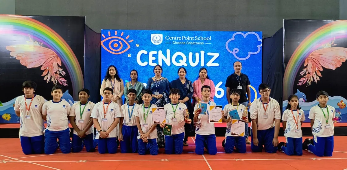 Group photo of students in white and blue uniforms kneeling in front of adults, holding certificates and a trophy, in front of a quiz stage backdrop at CPS (Katol Road).