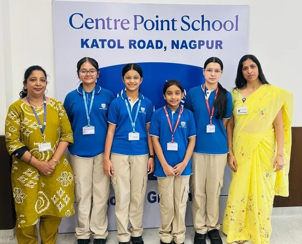 Group photo of four students in blue uniforms standing with two women teachers in front of a school banner, all facing the camera.