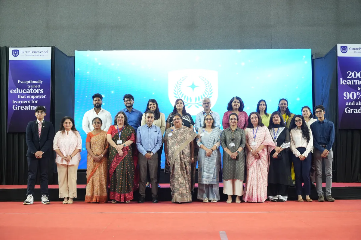 Group photo of adults and students posing in two rows on a stage at CPS (Katol Road)