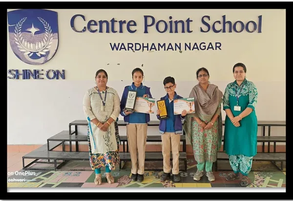 Two students holding certificates and plaques stand with three women teachers in front of CPS (Wardhaman Nagar) school name wall.