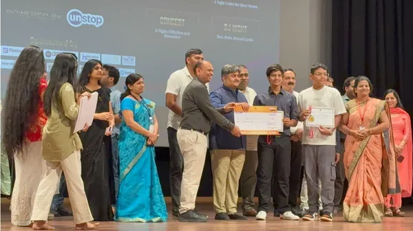 Prize ceremony on stage with adults and students, two men holding a large cheque and a student holding a certificate.