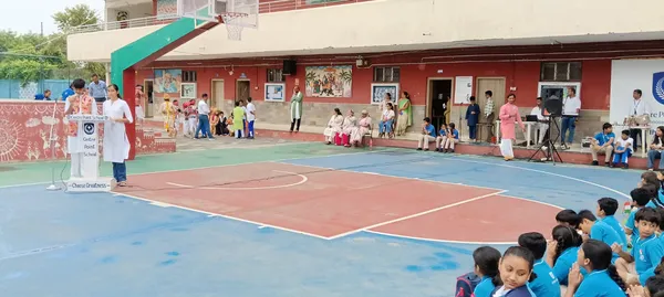 CPS (Wardhaman Nagar) school courtyard with speaker at podium, seated guests and rows of students in foreground