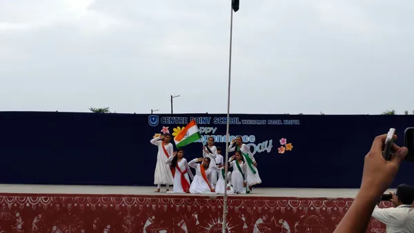 CPS (Wardhaman Nagar) girls in white dresses with tricolour sashes dancing on stage with flag
