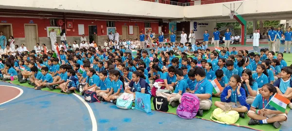 Large group of CPS (Wardhaman Nagar) students in blue uniforms seated on a courtyard floor, some holding small Indian flags
