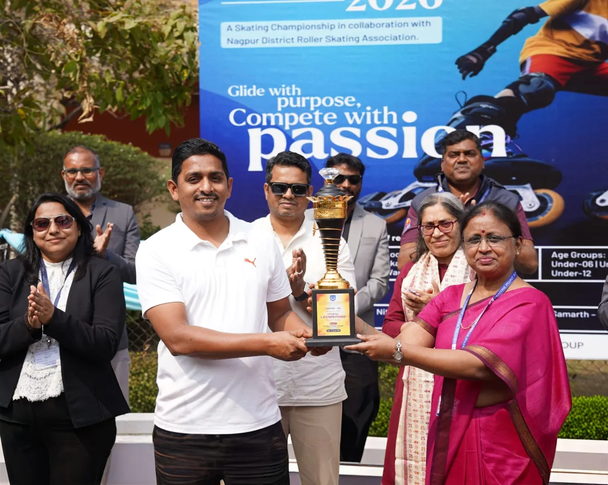 A man in a white polo shirt receives a trophy from a woman in a pink saree while others applaud in front of a CENSTRIDE 2026 skating championship banner.