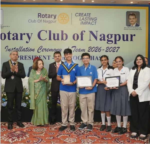 Group photo on stage of four students holding certificates and a plaque, with adults applauding beside them, in front of an installation ceremony banner.