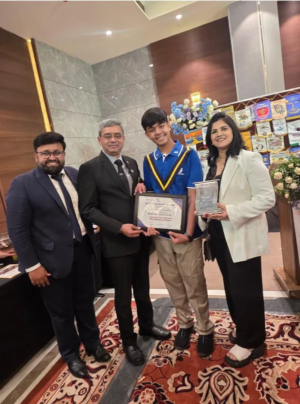 Four people, including a student in a blue polo with a sash, pose indoors holding a framed certificate and a plaque.