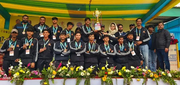 Group of about 20 players in dark tracksuits with medals on a podium behind flowers, holding up a trophy with officials.