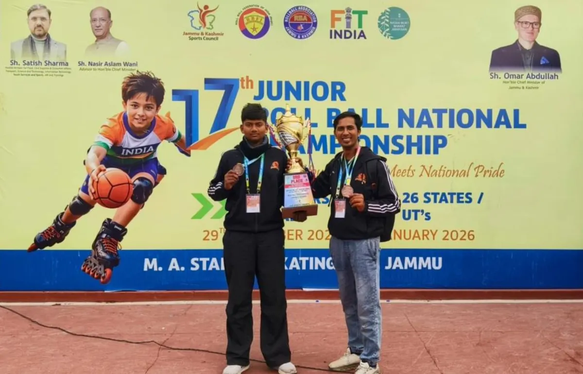 Two men in dark tracksuits with medals pose with a large trophy in front of a roll ball championship banner.