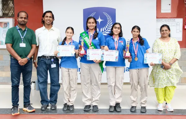 Group photo of four students in blue shirts holding certificates, trophies and medals, with three adults in front of a wall with a logo, CPS (Wardhaman Nagar)