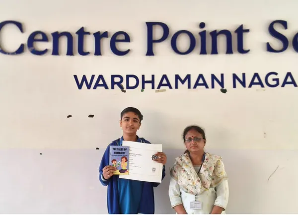 A student in a blue jacket holding a certificate and a book stands beside a woman in a floral top in front of CPS (Wardhaman Nagar) name wall.