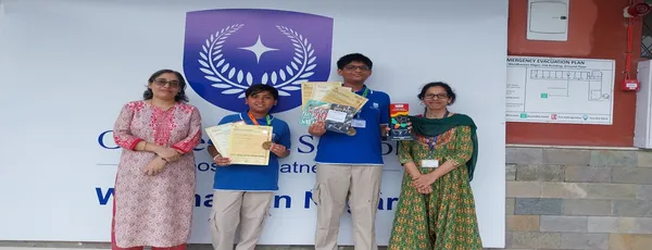 CPS (Wardhaman Nagar) students holding certificates and medals with two women in front of a school sign.