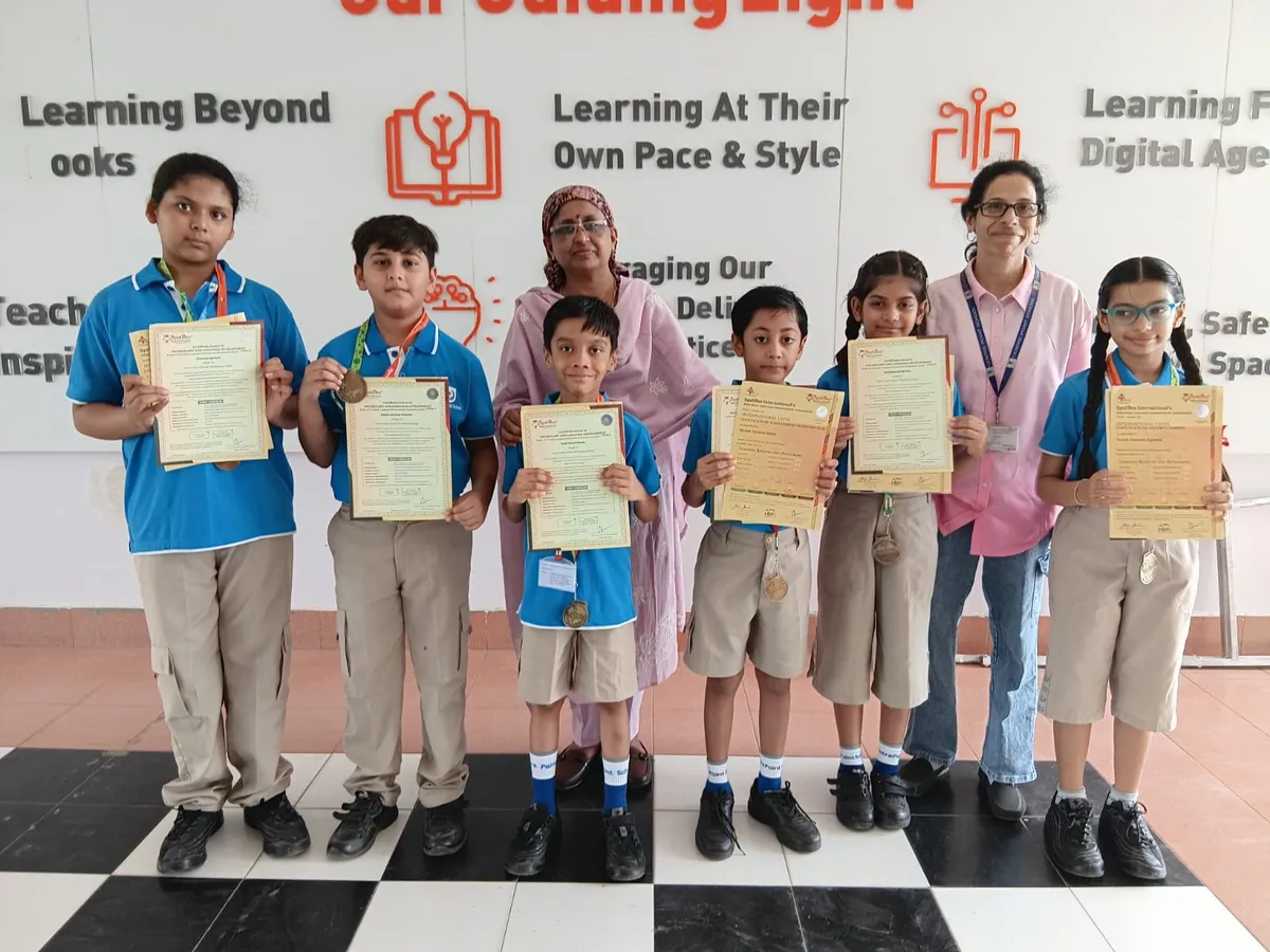 CPS (Wardhaman Nagar) students in blue shirts holding certificates and medals with two women indoors.