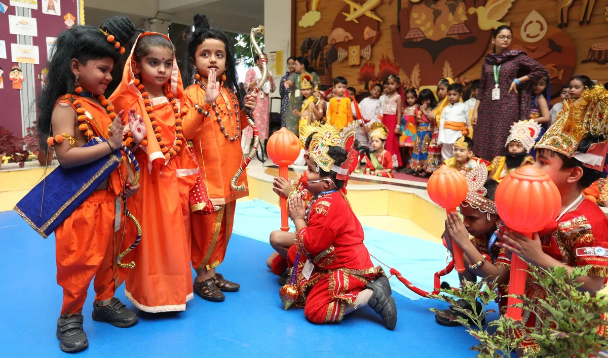 Young children in orange and red mythological costumes with crowns and props perform on a blue floor while other costumed children and a teacher look on. - DPS (Kamptee Road)