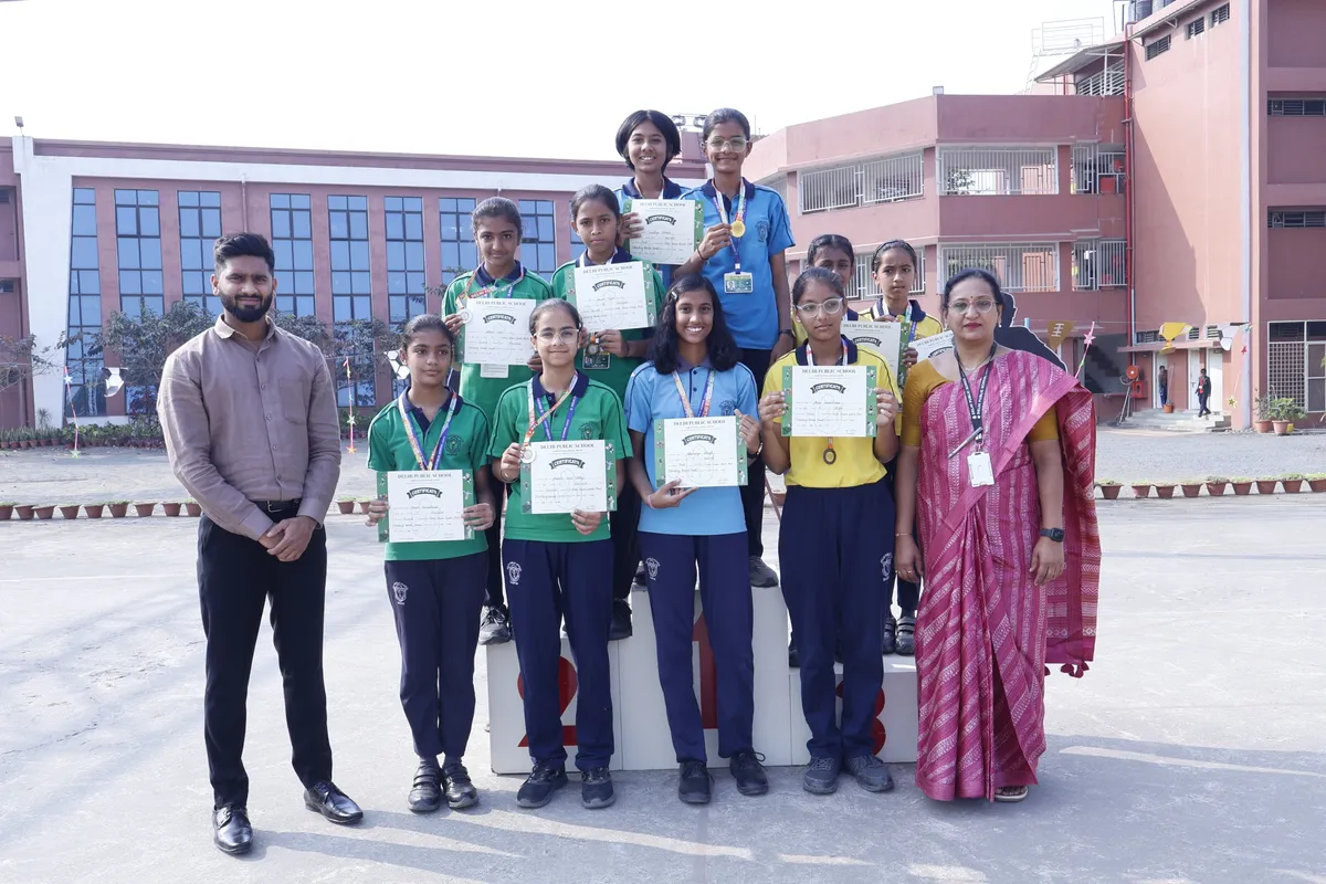 Students in school uniforms holding certificates and wearing medals with a man and a woman in front of DPS (Kamptee Road) building