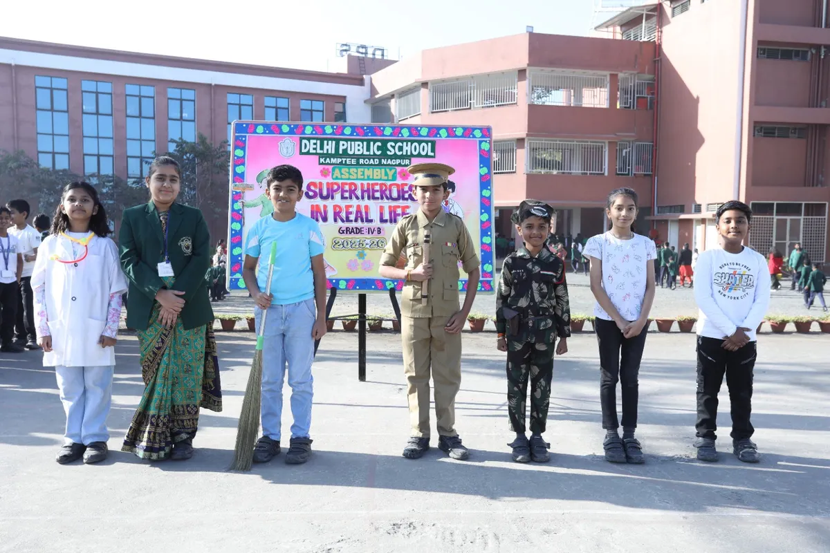 Seven students in costumes including doctor, policeman and soldier standing in a row beside an assembly signboard in a school courtyard at DPS (Kamptee Road)