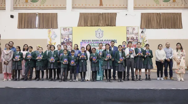 Group photo of students in green uniforms and adults standing on stage, many holding books, in front of a school banner.