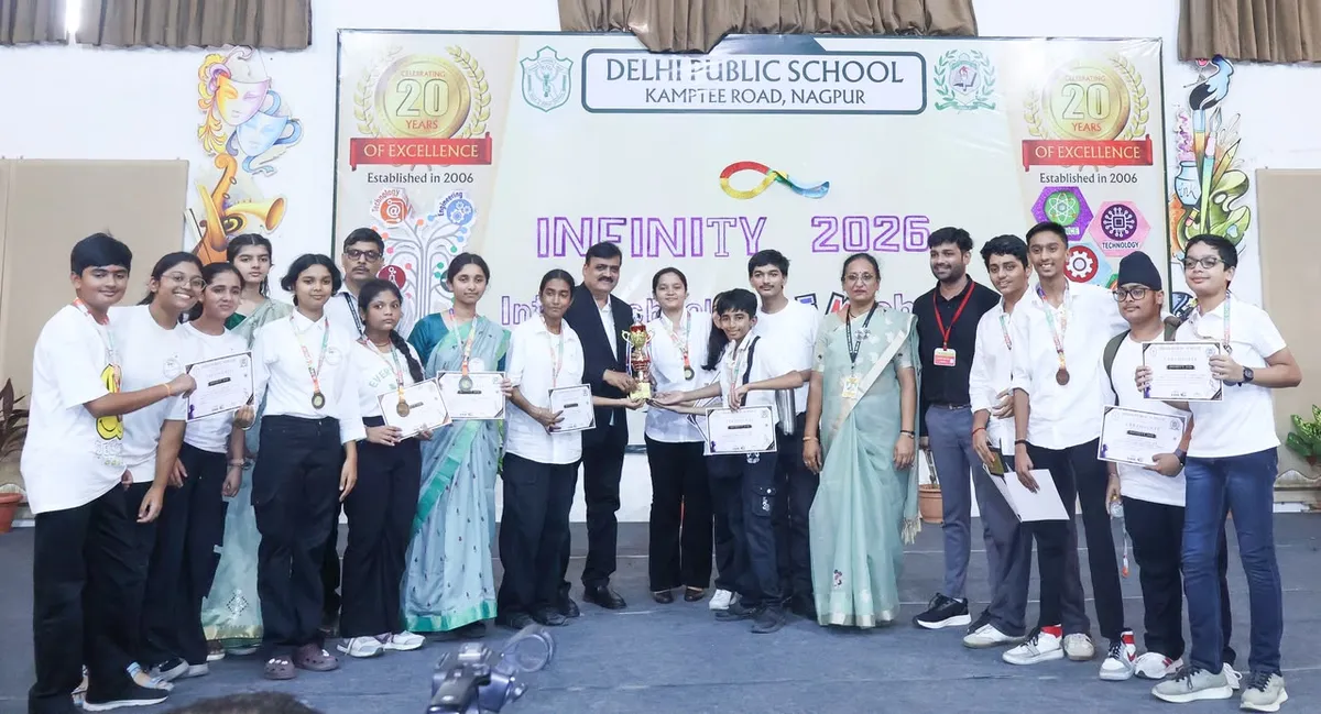Group photo of students and adults on a stage holding a trophy, medals and certificates in front of a school event banner at DPS (Kamptee Road).