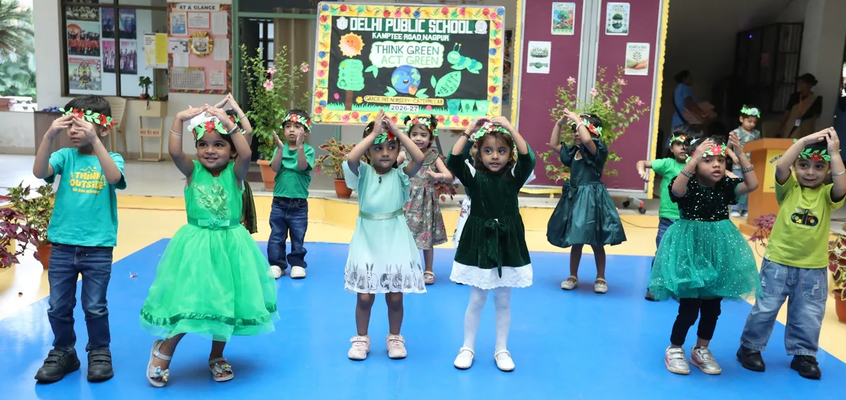 Young children in green outfits and leaf headbands dance on a blue mat in front of a decorated green-theme board. - DPS (Kamptee Road)