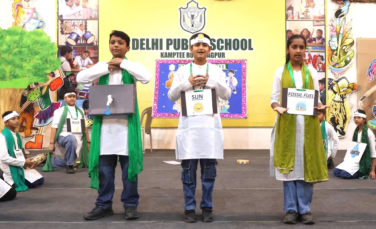 Students in white outfits with green scarves stand on a stage holding placards during a performance at DPS (Kamptee Road)