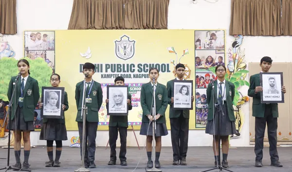 Students in school uniforms on stage at DPS (Kamptee Road) assembly, some at microphones and some holding framed portrait pictures