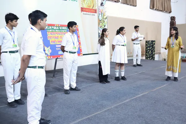 DPS (Kamptee Road) students performing a skit on a school stage with a decorated backdrop behind them.