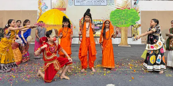 Students in colourful traditional costumes performing a stage play with flower petals scattered on the floor, with a school banner and decorated backdrop behind them. - DPS (Kamptee Road)