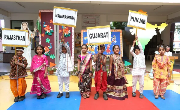 Eight young children in traditional regional costumes holding state name boards on a decorated stage with a map of India behind them. DPS (Kamptee Road)