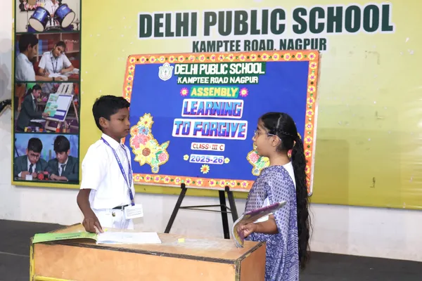 Two students perform on a stage at DPS (Kamptee Road) school assembly with books in hand.