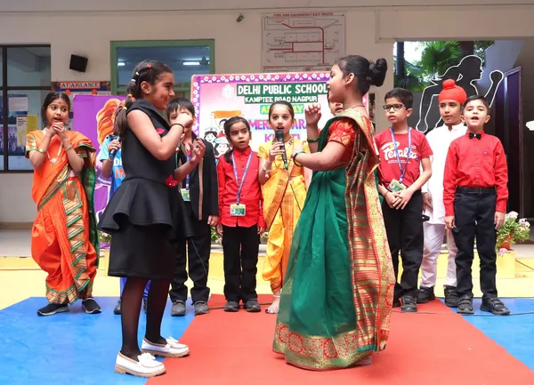 Schoolchildren in colourful traditional costumes performing on a stage with microphones in front of a decorated backdrop at DPS (Kamptee Road)