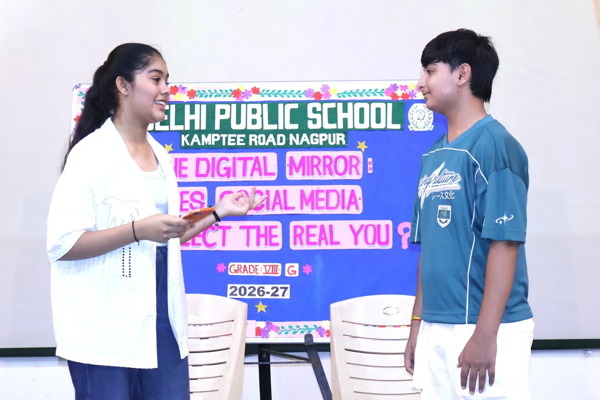 Two students performing on stage in front of a decorated board with DPS (Kamptee Road) school name and theme title