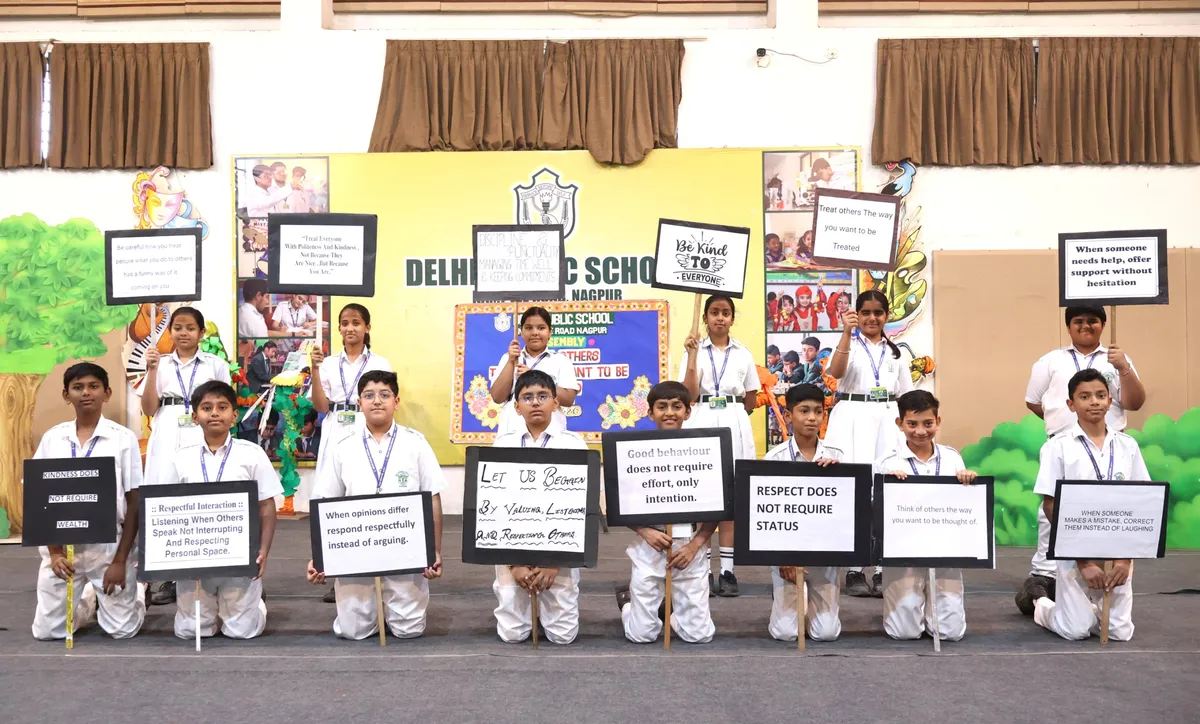 Group photo of about 16 Grade VI-D students in school uniform holding placards with messages, in front of a decorated stage backdrop at DPS (Kamptee Road)