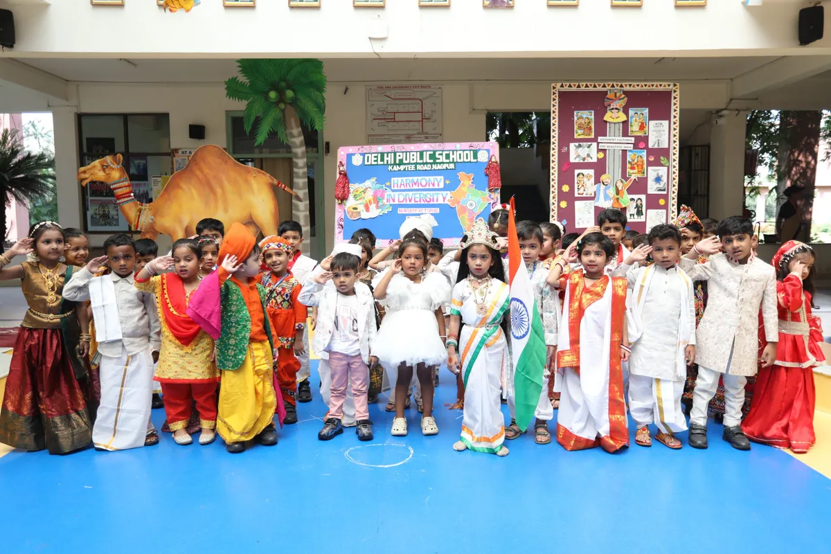 Group of young children in colourful traditional costumes saluting beside an Indian flag in a school courtyard at DPS (Kamptee Road)