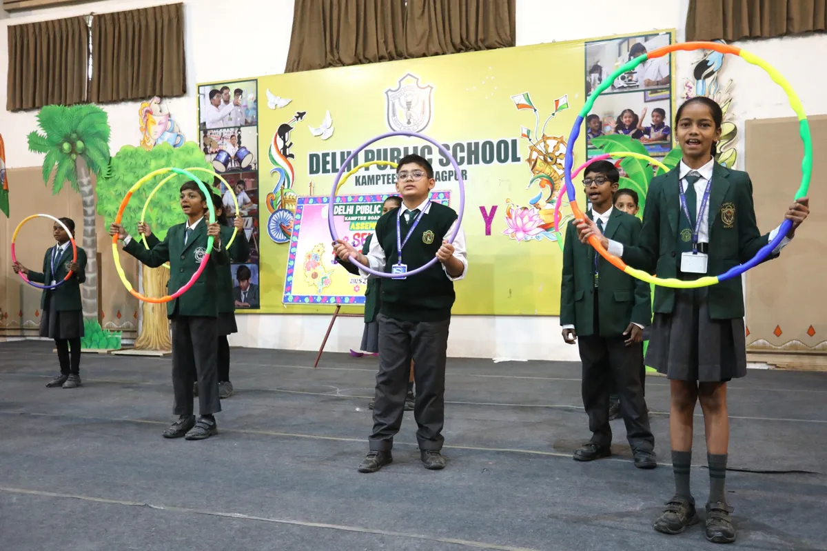 DPS (Kamptee Road) students in school uniforms with hula hoops on stage in front of decorated backdrop with school name banner