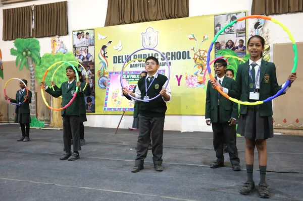 DPS (Kamptee Road) students in school uniforms with hula hoops on stage in front of decorated backdrop with school name banner