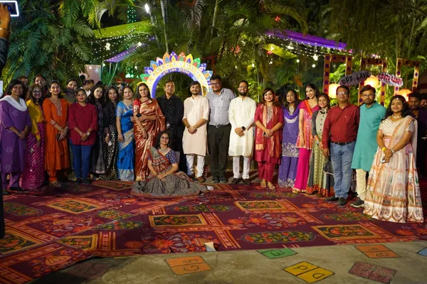 Large group of adults in colorful traditional clothing posing outdoors on a patterned carpet under a decorative arch with lights. - DPS (Lava)