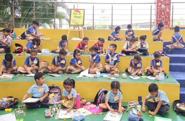 Young students in uniforms sit on colorful tiered steps doing drawing and craft activities at DPS (Mihan).