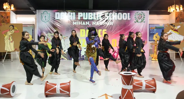 A group of girls in black costumes dance on stage with a central performer painted blue, with drums in the foreground at DPS (Mihan).