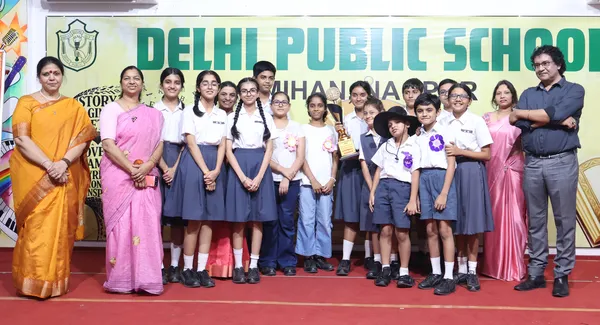 Group photo of students in school uniform with a trophy, flanked by adults, on a red-carpeted stage. - DPS (Mihan)